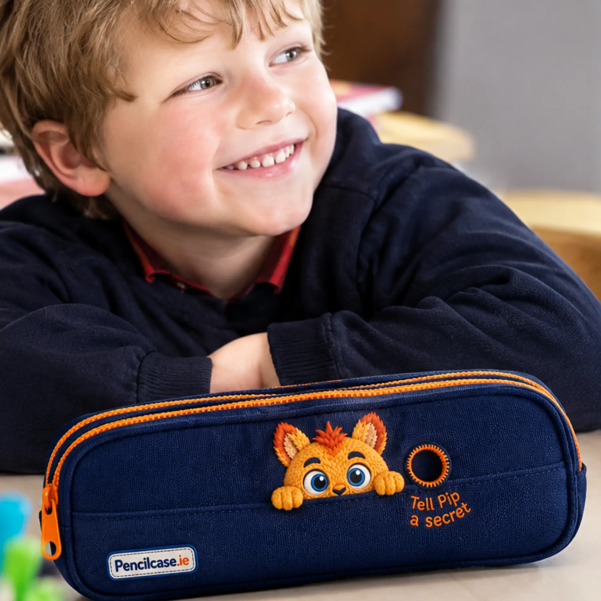 A boy smiling beside his Pip pencil case at his school desk